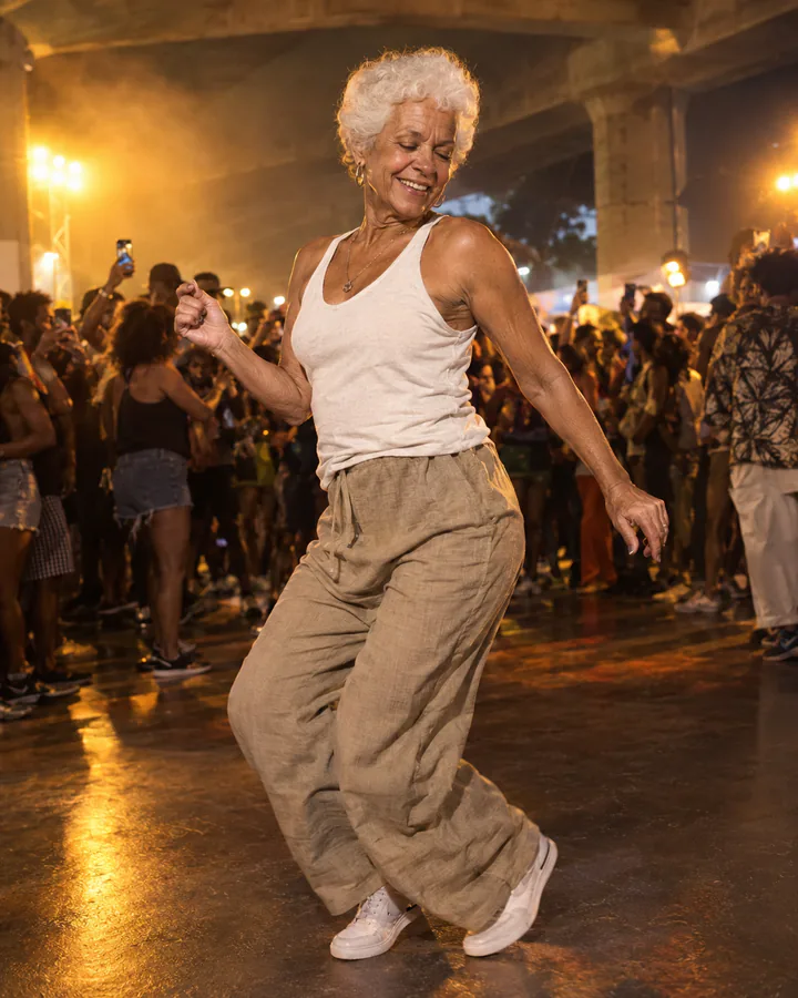 An older dancer with white hair smiling in a packed night crowd